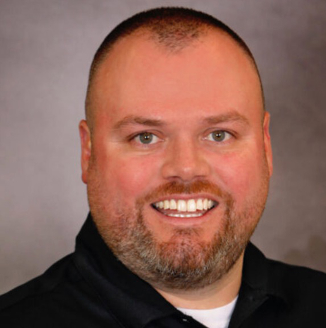 man with short hair and beard smiling on a gray background