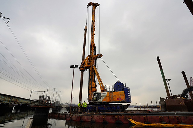 a large drill towers over men standing on a platform by the river