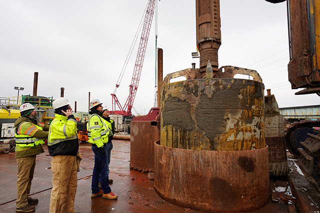 three men stand next to massive drill and bucket